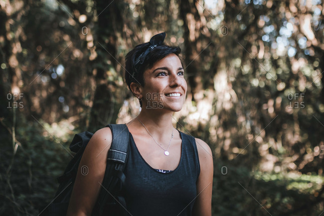 Portrait of a beautiful woman with short hair and a beautiful smile admiring nature in the forest while hiking wearing a backpack in the woods