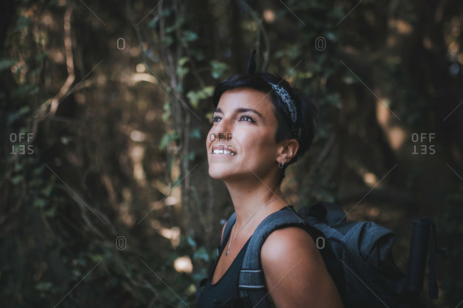 Portrait of a beautiful woman smiling with short hair and a beautiful smile admiring nature in the forest while hiking wearing a backpack
