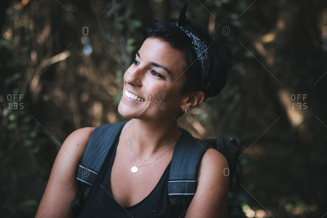 Portrait of a beautiful woman smiling with short hair and a beautiful smile admiring nature in the forest while hiking wearing a backpack