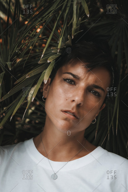 Portrait of an attractive and beautiful serious woman with short hair looking at the camera surrounded by green leaves