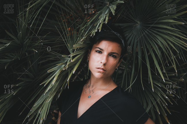 Portrait of a beautiful serious woman with short hair looking at the camera with plants in the background