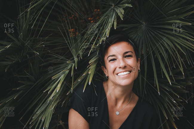 Portrait of a beautiful joyful woman with a beautiful smile and short hair looking at the camera smiling with plants in the background