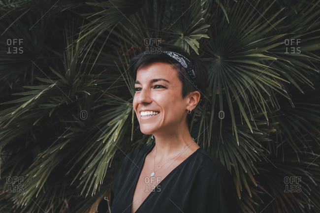 Portrait of a beautiful joyful woman with a beautiful smile and short hair looking away smiling with plants in the background