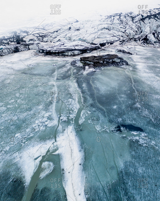 Aerial view of glacier Solheimajokull, with black and white patterns created by volcanic ash trapped in the ice, and its frozen glacial lagoon, South Iceland.