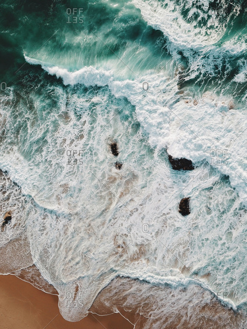 Aerial view of huge waves crashing on the coastline. Amazing turquoise ocean and golden sand. Praia da Crismina, Guincho, Portugal