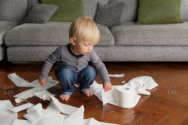 Cute toddler making mess with toilet paper in living room
