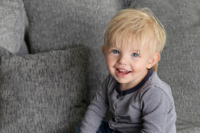 Portrait of smiling blue-eyed toddler on grey couch