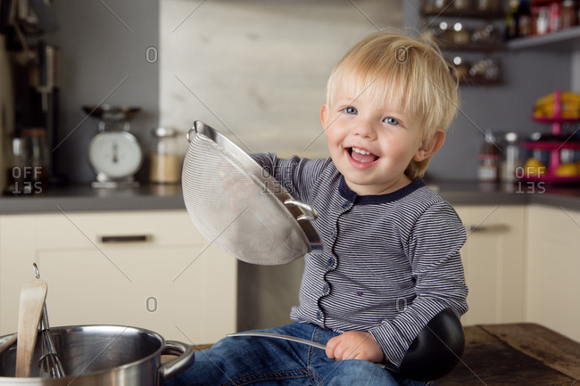 Baby boy playing on kitchen counter with strainer over his head Stock Photo