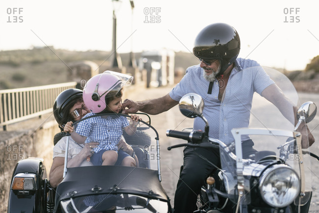 Mature couple in a sidecar travel with their two-year-old grandson and park to rest.