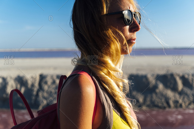 Pensive middle aged female traveler in sunglasses looking at sunset while standing on blurred background of pink lake in Las Coloradas, Mexico