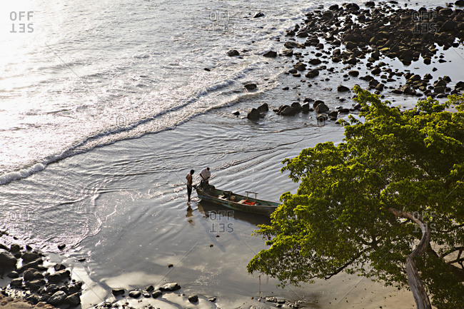 Bird's eye view over beach with two fishermen loading up a boat in Sayulita, Nayarit, Mexico