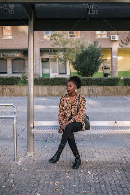 Young black woman sitting waiting for the bus at a city bus stop