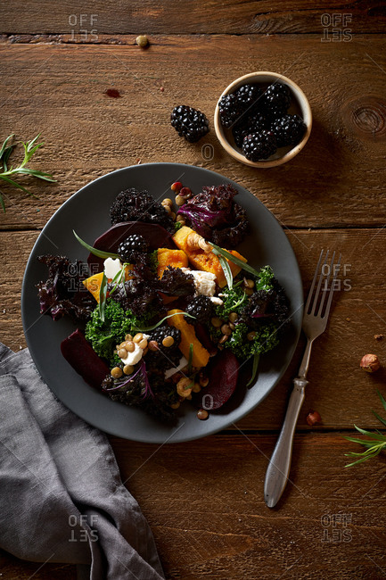 Vegetarian salad with roasted butternut squash, kale, beetroot and blackberries garnished with tarragon leaves.