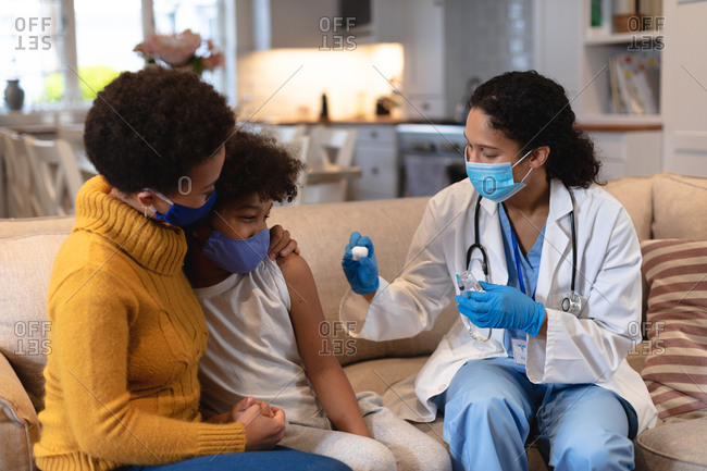 Mixed race girl and mother wearing face masks with mixed race female doctor preparing flu vaccine