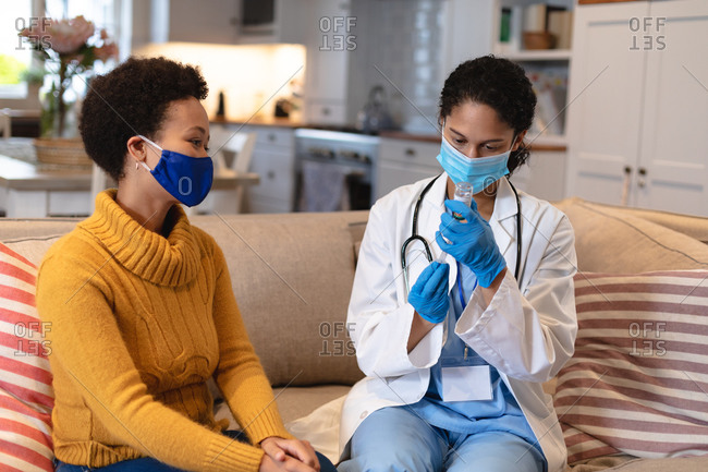 Mixed race woman wearing face mask talking to a mixed race female doctor sitting on couch