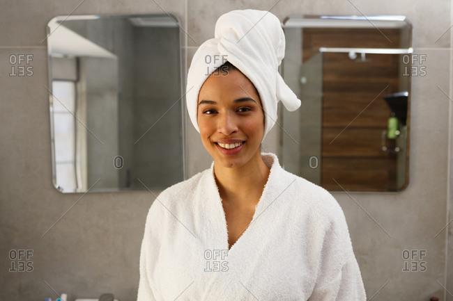 Portrait of smiling mixed race woman wearing bathrobe and towel on head in bathroom