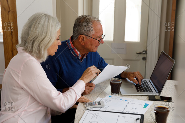 Stressed senior caucasian couple using laptop and calculating finances at home