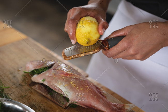 Mid section of chef grating lemon rind on roasted fish in restaurant kitchen