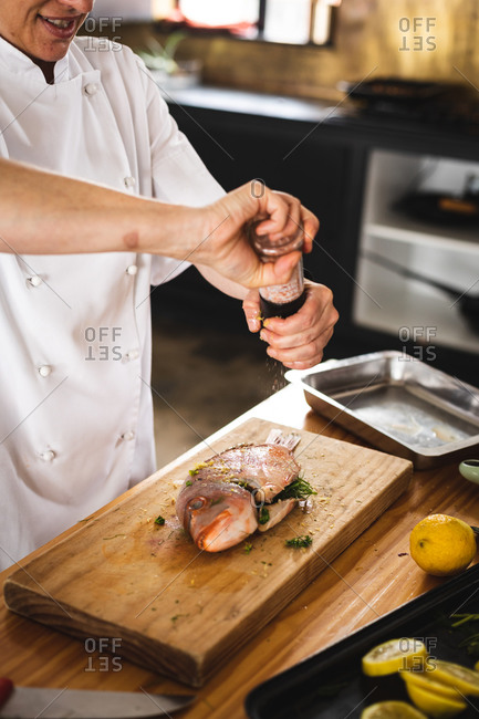 Mid section of chef grinding pepper over roasted fish in restaurant kitchen