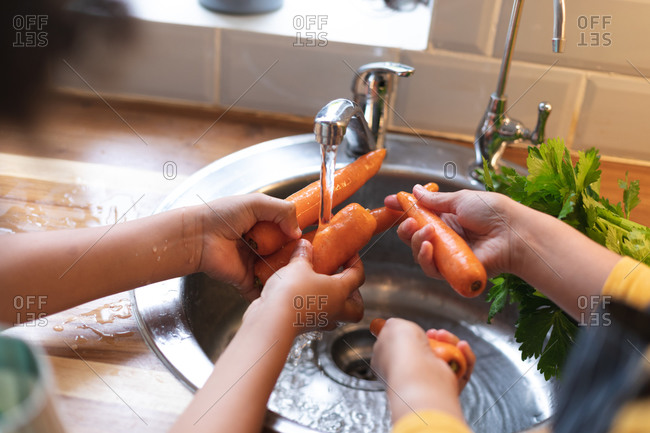 Mixed race lesbian couple preparing food washing carrots in kitchen sink