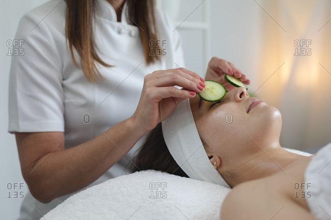 Caucasian woman lying back while beautician puts cucumbers on her face