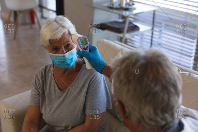 Doctor taking temperature of senior caucasian woman wearing face mask