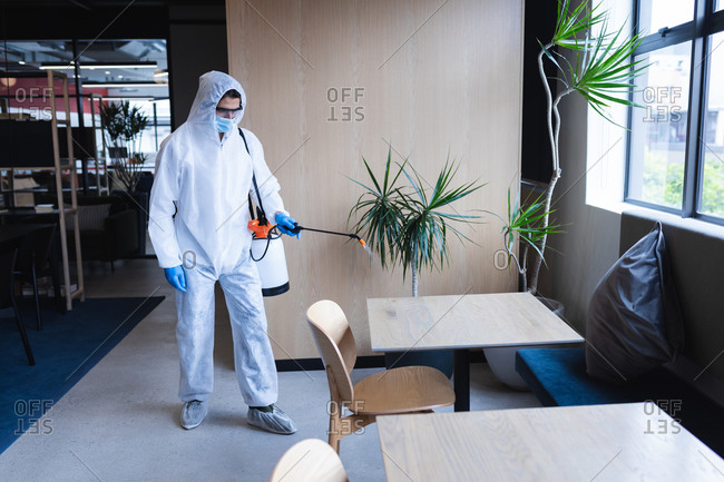Health worker in protective clothing spraying disinfectant in office