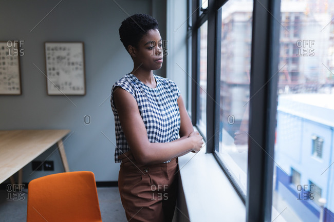 Pensive african american woman standing by window in creative office