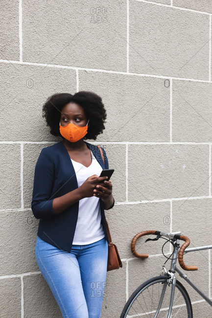 African american woman wearing face mask using smartphone in street