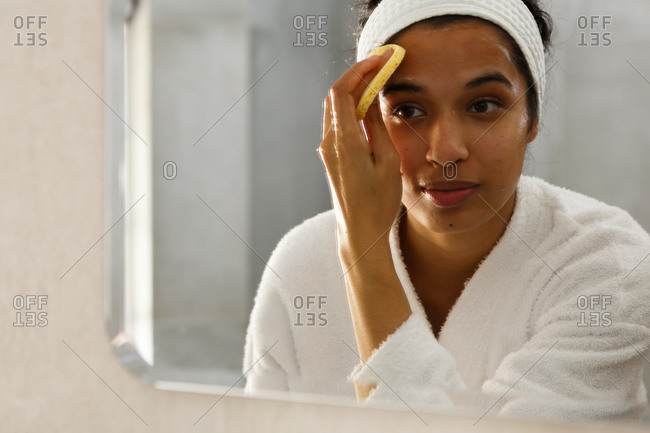 Mixed race woman reflected in mirror cleansing face in bathroom
