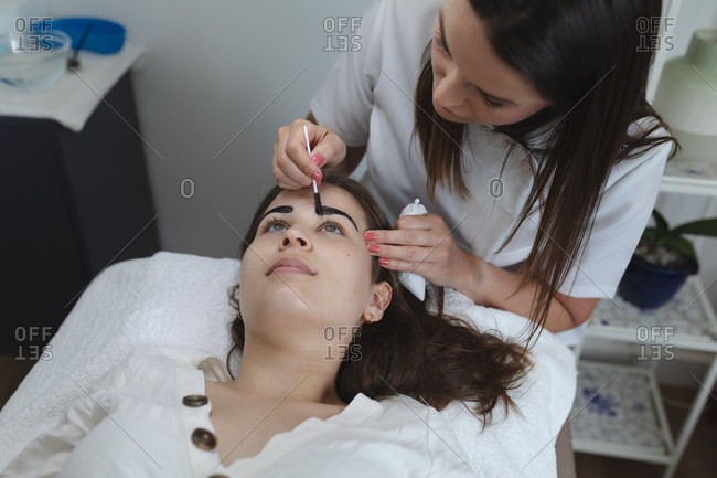 Caucasian woman lying back while beautician dyes her eyebrows