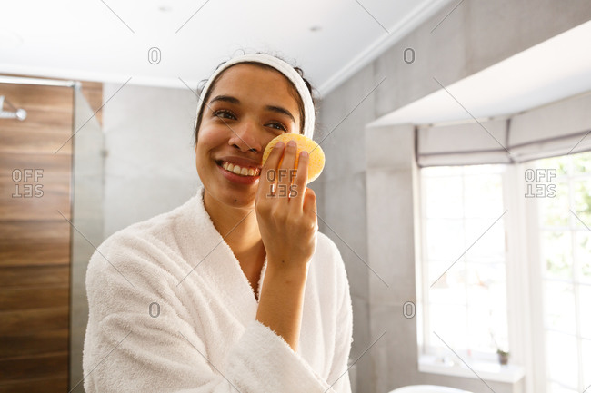 Mixed race woman looking in mirror cleansing face in bathroom