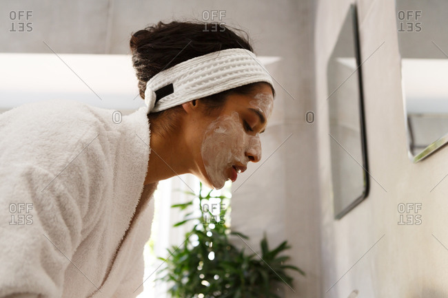 Mixed race woman wearing face cream and bathrobe in bathroom