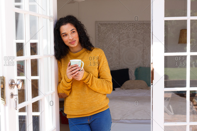 Mixed race woman standing in doors drinking cup of coffee