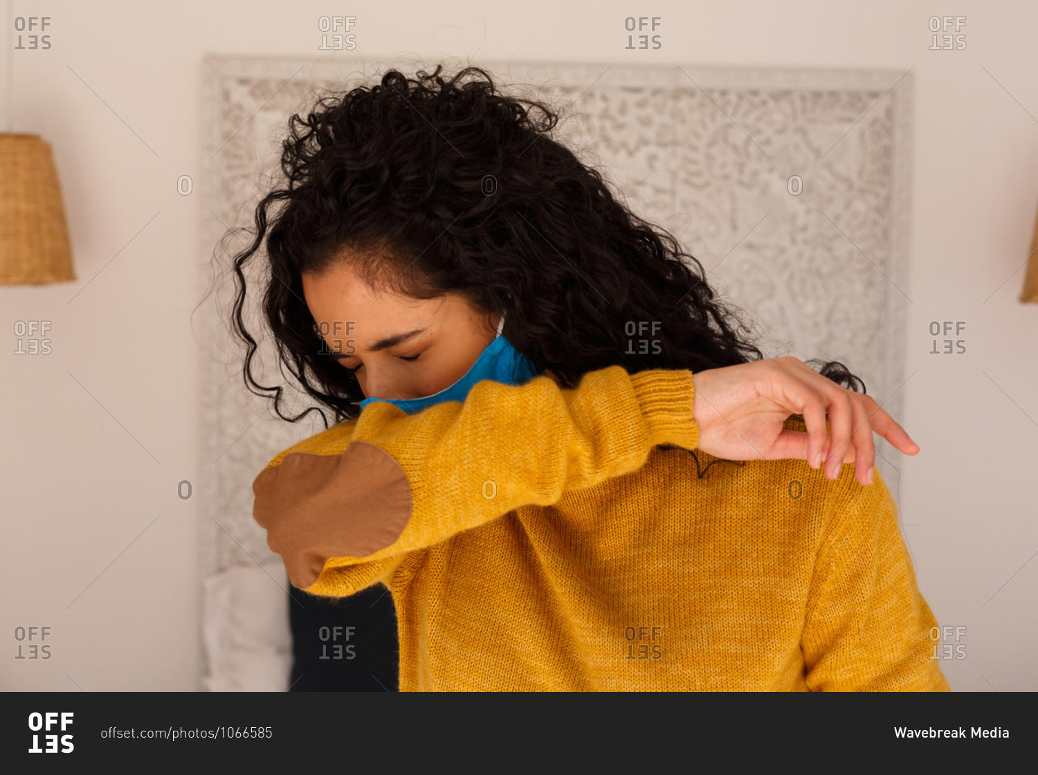 Mixed race woman wearing face mask coughing into arm
