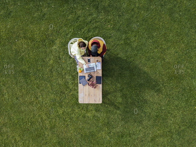 Aerial view of man and woman working together on laptop at coffee table set on green lawn