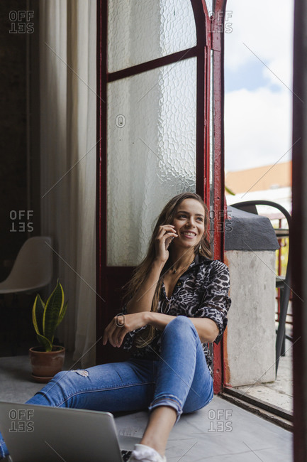 Smiling creative businesswoman talking on mobile phone while sitting at doorway in office