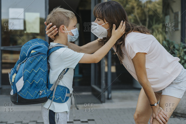 Mother and son wearing protective mask standing face to face in front of school building