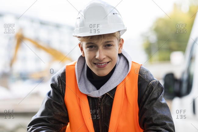 Smiling teenage construction trainee wearing hardhat and reflective clothing at site