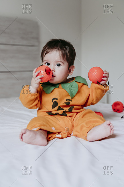 Cute male toddler playing with pumpkin Halloween toy while sitting on bed at home