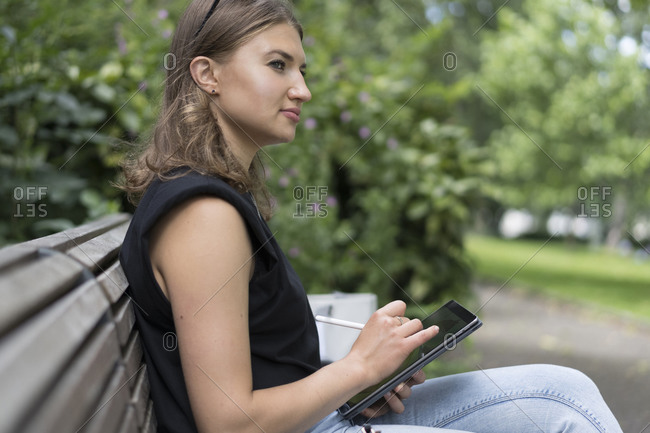 Young woman drawing on graphic tablet while looking away sitting in public park