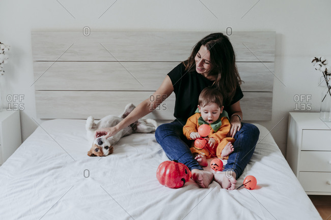 Mother sitting with son wearing Halloween costume and dog lying on bed at home