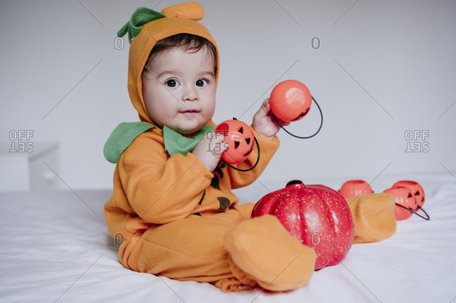 Baby boy wearing Halloween costume playing with pumpkin toy sitting at home