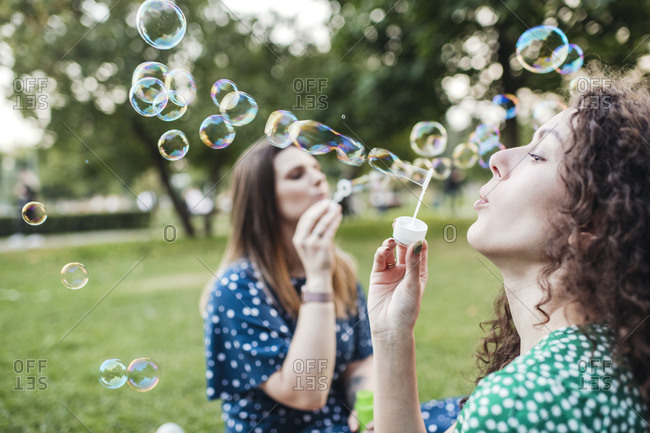 Beautiful female friends enjoying while blowing bubbles from wands at park