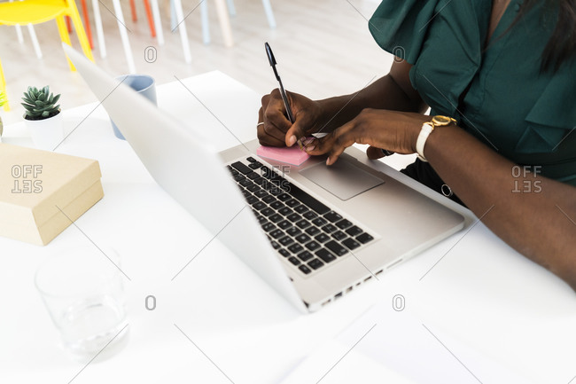 Businesswoman writing on adhesive note while working on laptop at office