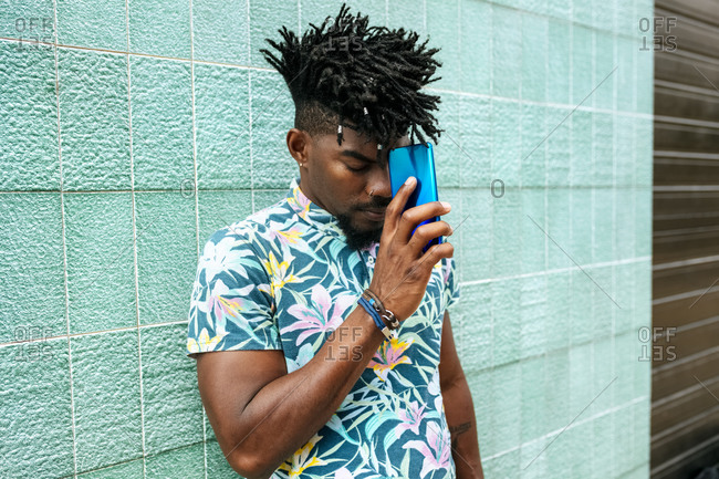 Mid adult man with locs holding mobile phone while standing against wall