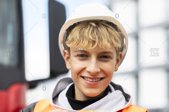 Smiling blond male teenage trainee wearing hardhat at construction site