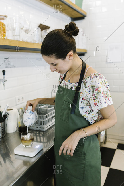 Barista pouring milk in coffee while standing in kitchen at coffee shop