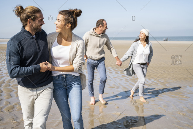 Smiling young couple walking with mature couple in background at beach