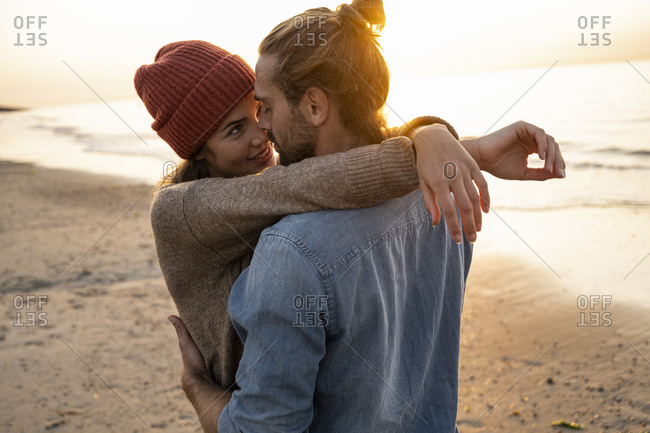Smiling young woman embracing while looking at boyfriend during sunset